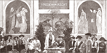 Fot av Bertha von Suttner som står och håller tal i mitten av bilden, omkring henne sitter och står kvinnor. Bakom henne syns väggmålningar och texten Vrede door Recht - Fred genom Rättvisa